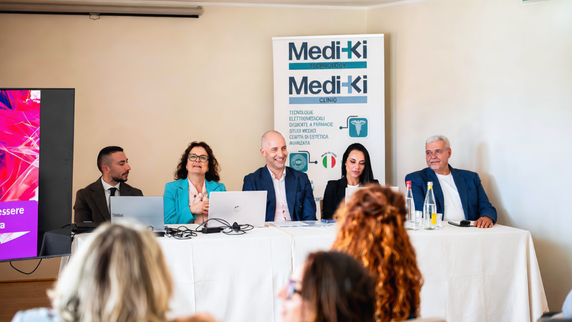 Panel di relatori durante un evento Mediki Technology, con i roll-up MediKi sullo sfondo